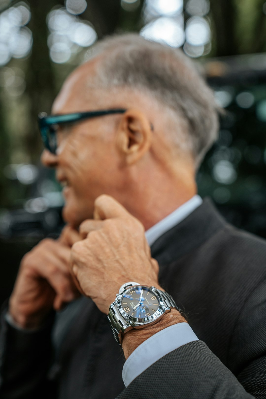 In this stylish composition, a man meticulously adjusts his bowtie, while a captivating luxury watch takes center stage. The attention to detail and the juxtaposition of the refined bowtie and the exquisite timepiece embody elegance and sophistication. by Watch Brands a man in a suit and glasses is looking away from the camera
